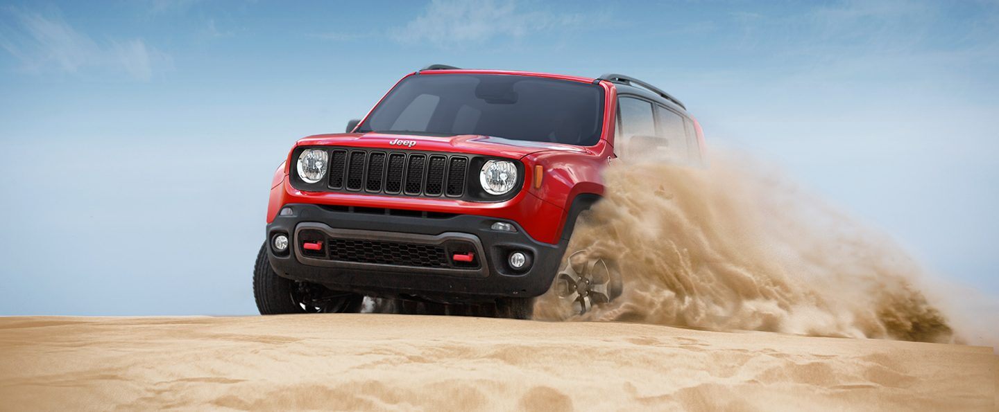 The 2021 Jeep Renegade being driven on sandy terrain, kicking up sand from the driver-side tires.