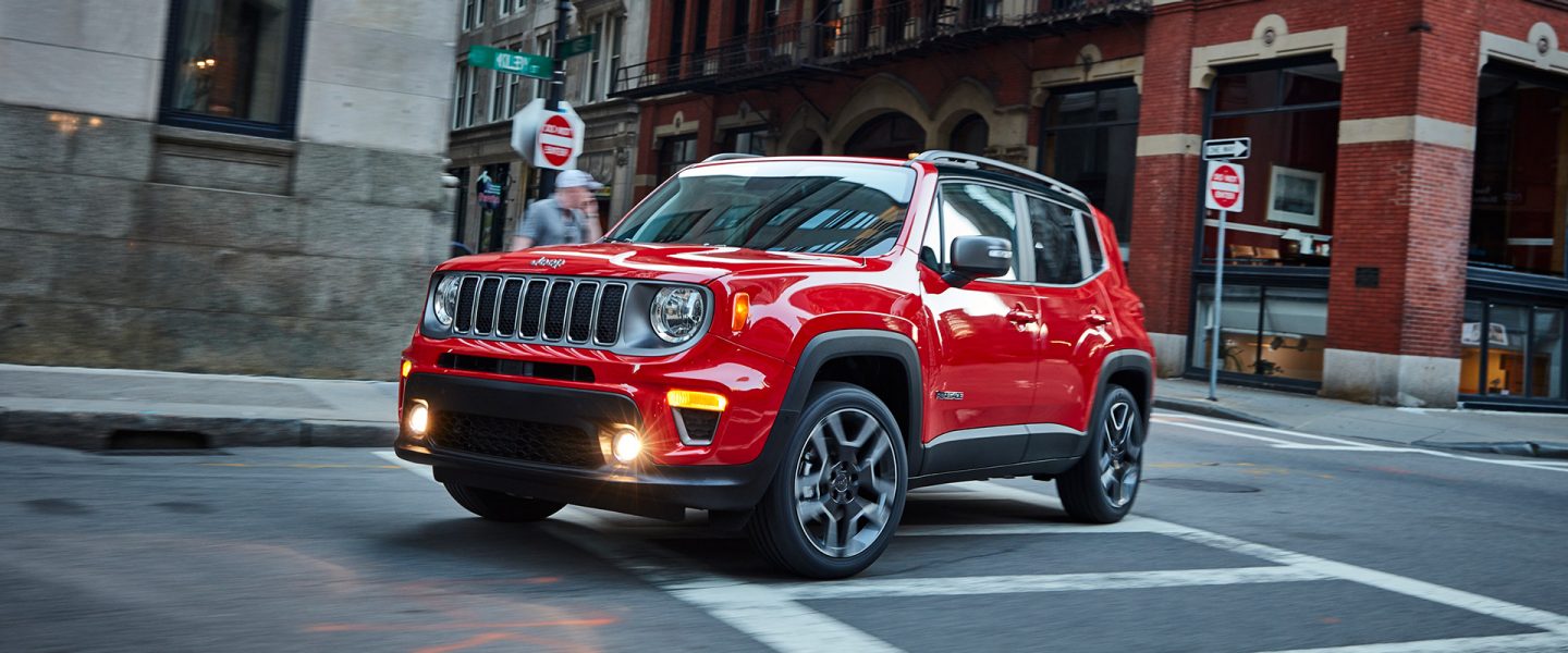 A red 2021 Jeep Renegade turning a corner on a busy city street.