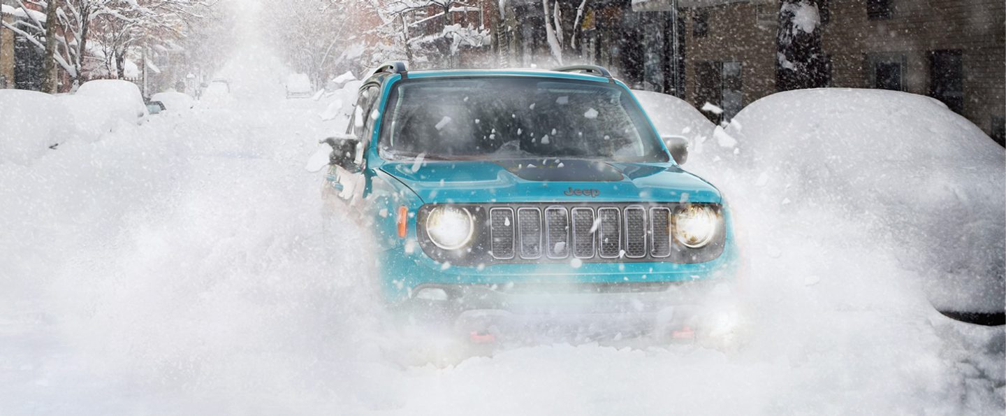 A head-on view of a 2021 Jeep Renegade being driven on a neighborhood street through a heavy snowstorm.